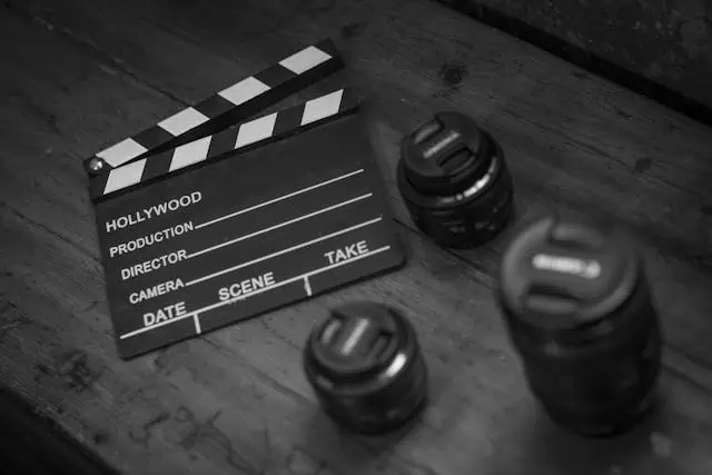 A grayscale of a clapperboard beside a camera lens
